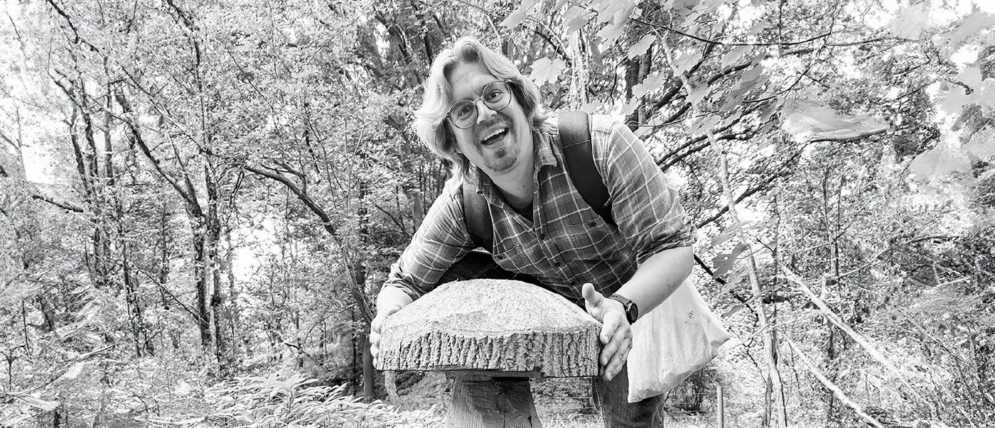 Author smiling with a carved wooden mushroom made from a log.